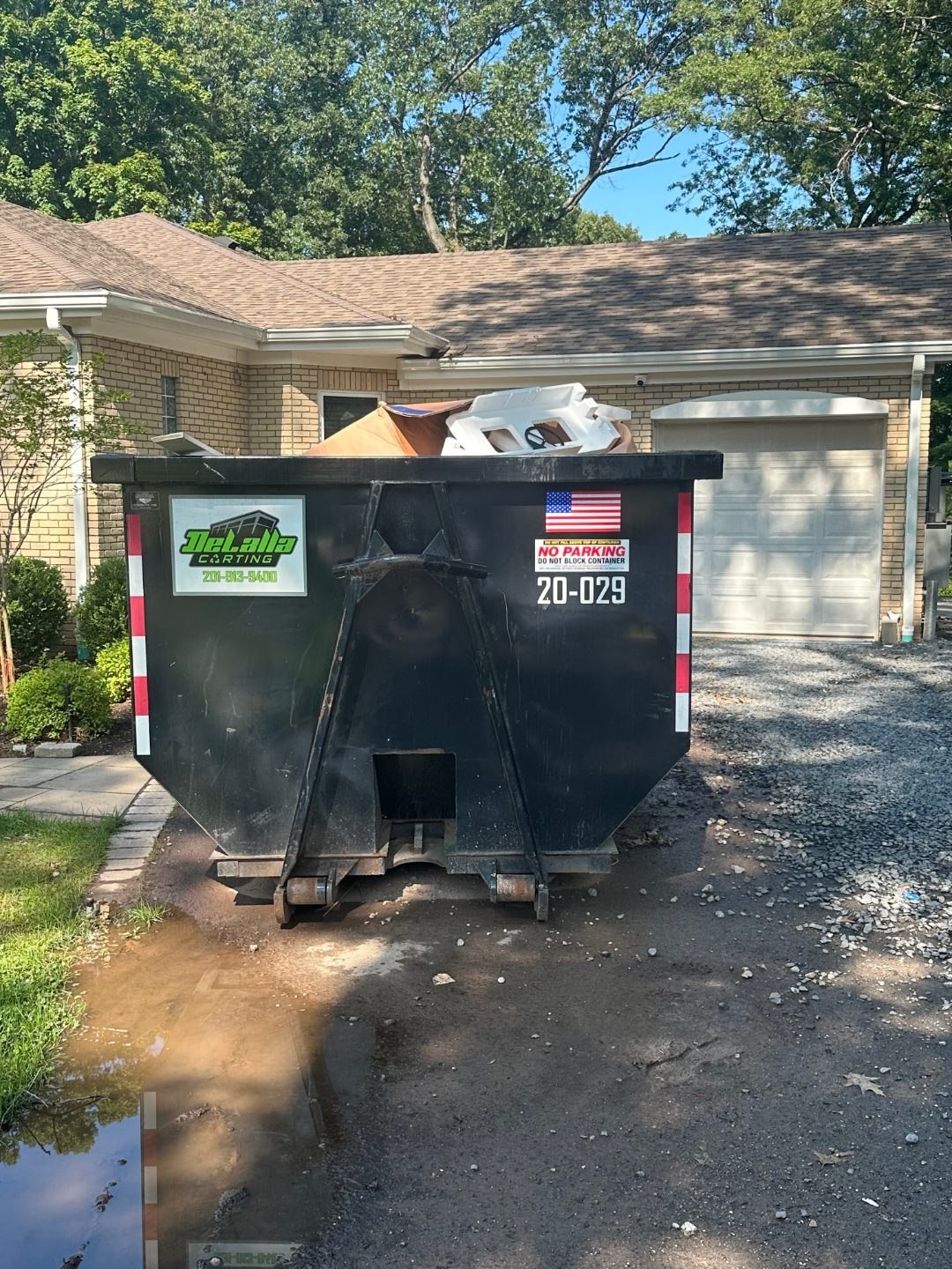 20-yard dumpster loaded with packing cardboard and foam on a gravel driveway in Paramus, NJ.